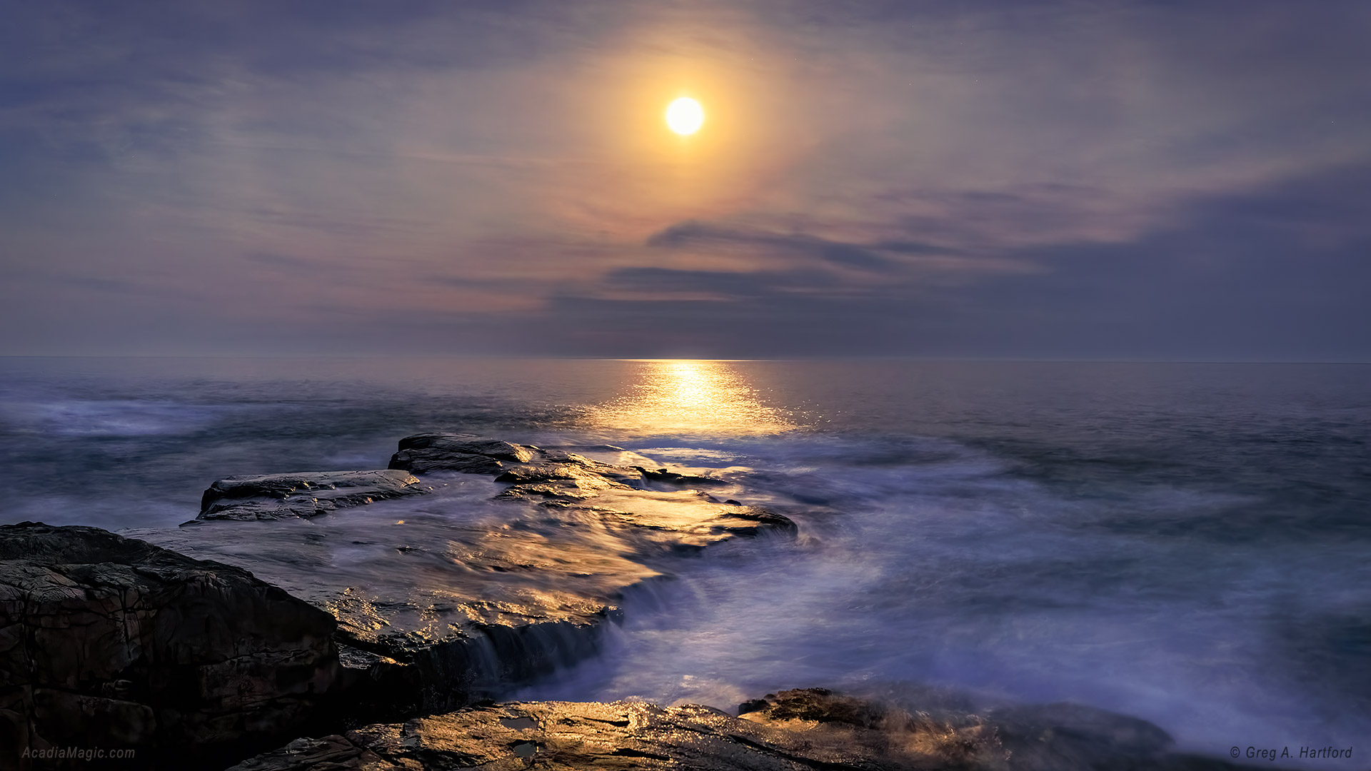 The moon shines through the light haze and reflects on the ocean's surface at Schoodic Point in Acadia National Park.
