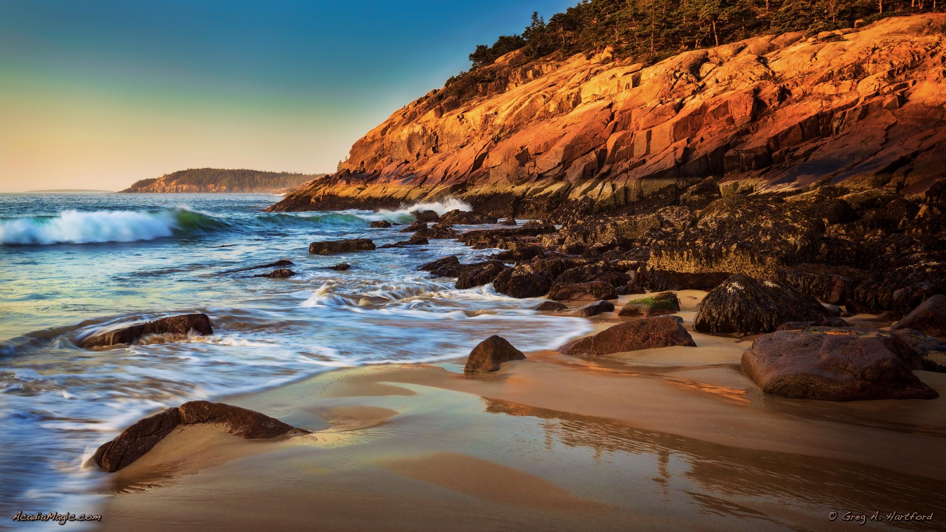 Sunrise at Sand Beach in Acadia National Park creates a warm glow on the granite cliffs.